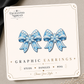 Blue snowflake bow graphic earrings with white snowflake and icing-style details on an Enchanted Nomad Designs display card.