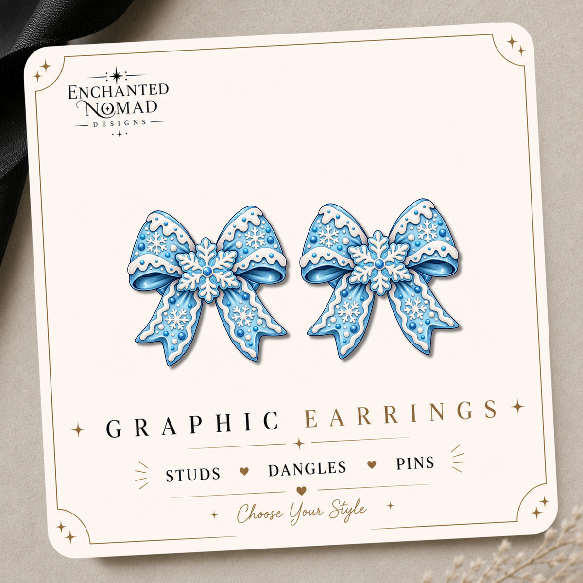 Blue snowflake bow graphic earrings with white snowflake and icing-style details on an Enchanted Nomad Designs display card.