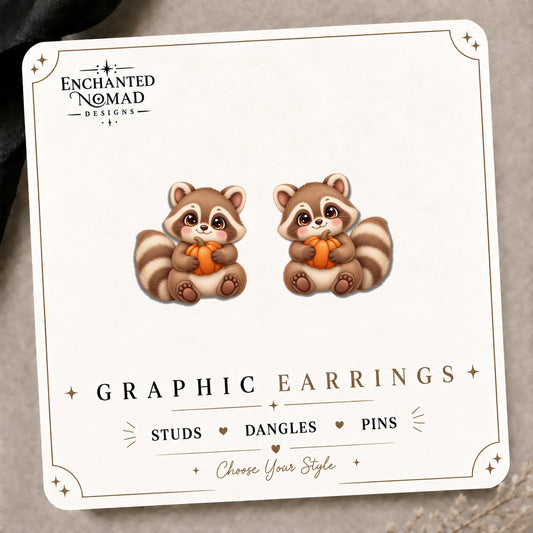 Raccoon Holding Small Pumpkin Stud Earrings on the tilted Enchanted Nomad Designs card
